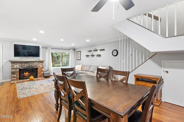 dining area featuring ceiling fan, ornamental molding, a fireplace, and light hardwood / wood-style floors