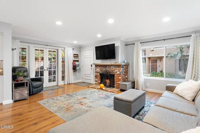 living room featuring crown molding, a brick fireplace, light hardwood / wood-style floors, and french doors