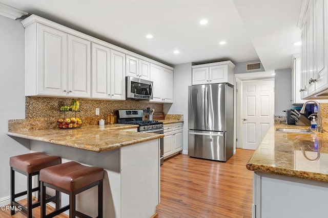 kitchen with appliances with stainless steel finishes, white cabinetry, sink, kitchen peninsula, and light stone countertops