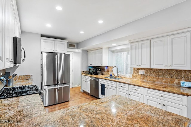 kitchen featuring sink, appliances with stainless steel finishes, white cabinetry, light stone counters, and tasteful backsplash