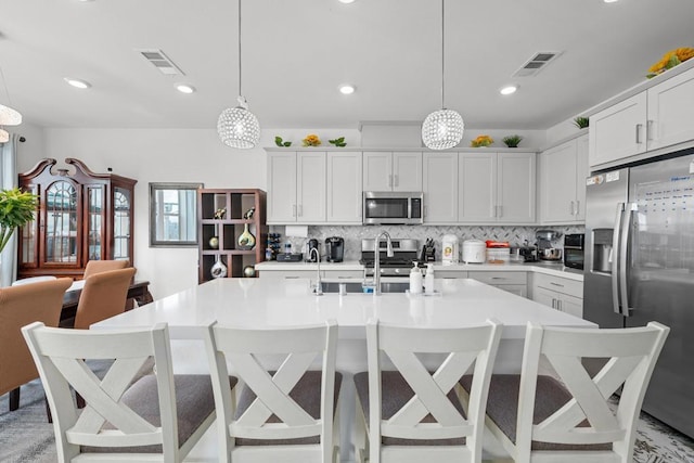 kitchen featuring appliances with stainless steel finishes, a kitchen breakfast bar, hanging light fixtures, and a kitchen island with sink