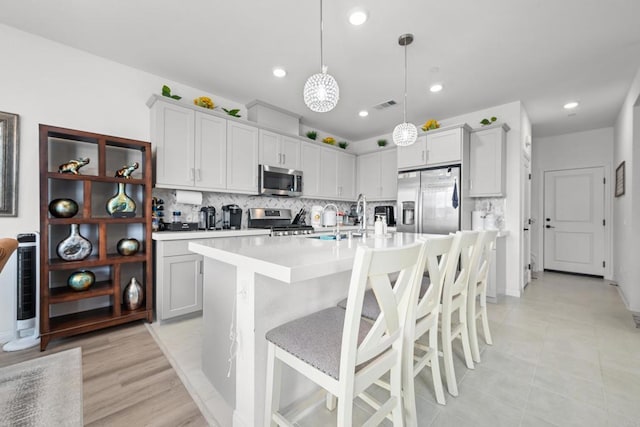 kitchen with an island with sink, stainless steel appliances, sink, a kitchen breakfast bar, and pendant lighting