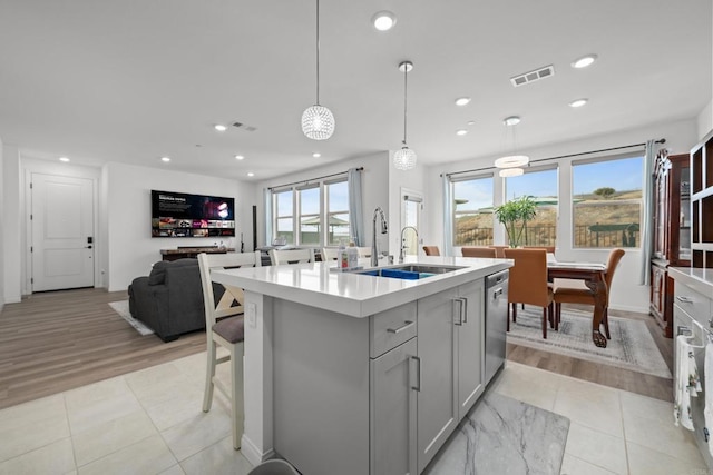 kitchen featuring sink, gray cabinetry, decorative light fixtures, stainless steel dishwasher, and a kitchen island with sink