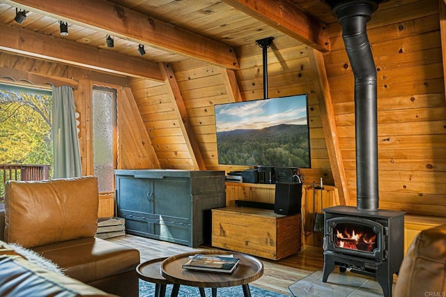 interior space featuring wood walls, light hardwood / wood-style flooring, wooden ceiling, a wood stove, and beam ceiling