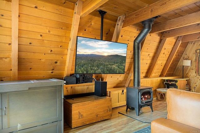 interior space featuring light hardwood / wood-style flooring, wooden walls, lofted ceiling with beams, wooden ceiling, and a wood stove