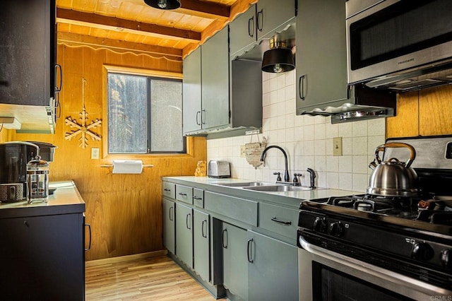 kitchen with appliances with stainless steel finishes, sink, backsplash, beam ceiling, and light hardwood / wood-style flooring