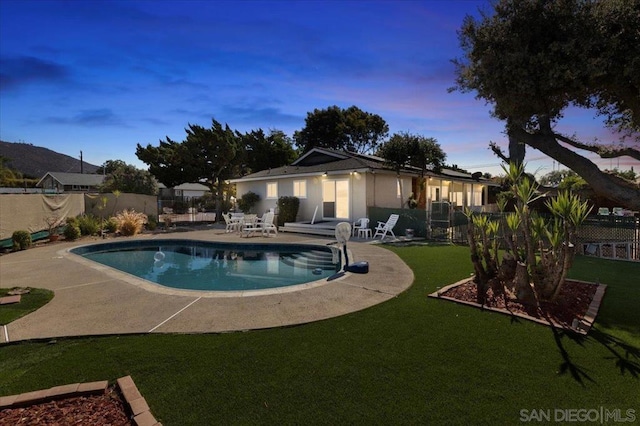 pool at dusk with a yard and a patio area