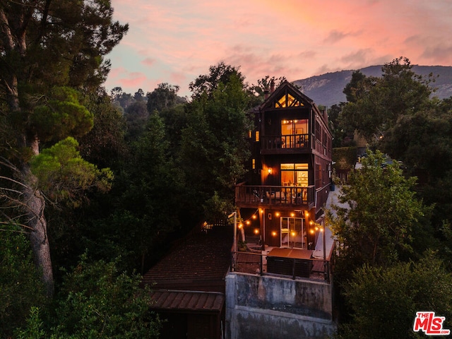 back house at dusk featuring a mountain view, a patio area, and a balcony