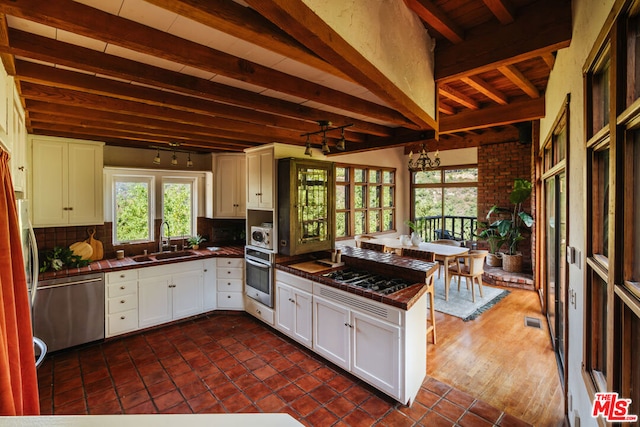 kitchen with sink, white cabinets, kitchen peninsula, stainless steel appliances, and beam ceiling