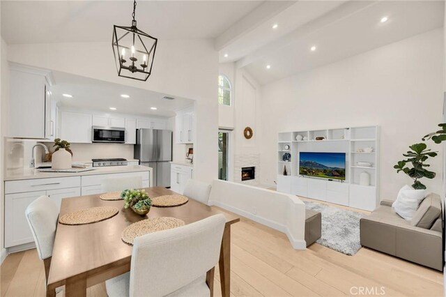 dining space featuring sink, a chandelier, high vaulted ceiling, light wood-type flooring, and beam ceiling