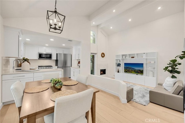 dining room with high vaulted ceiling, sink, light wood-type flooring, a chandelier, and beam ceiling