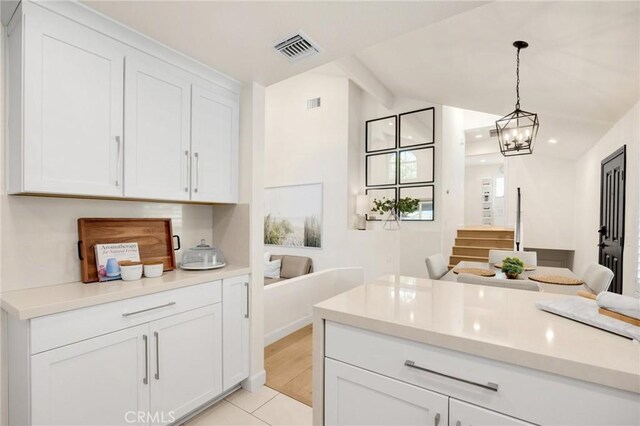 kitchen with light tile patterned flooring, decorative light fixtures, lofted ceiling with beams, white cabinets, and a chandelier