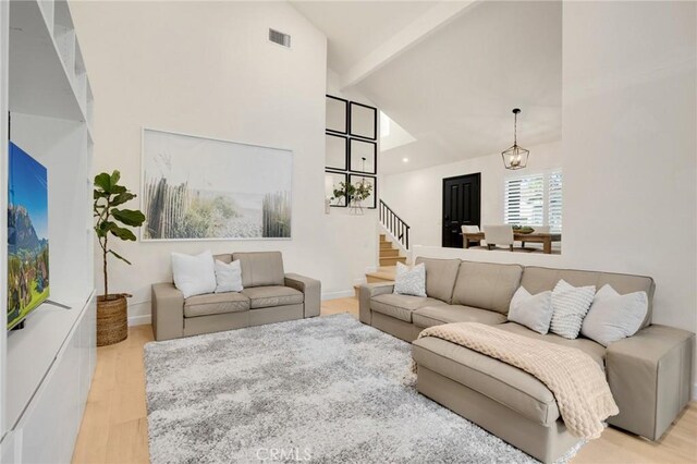 living room with an inviting chandelier, high vaulted ceiling, beamed ceiling, and light wood-type flooring