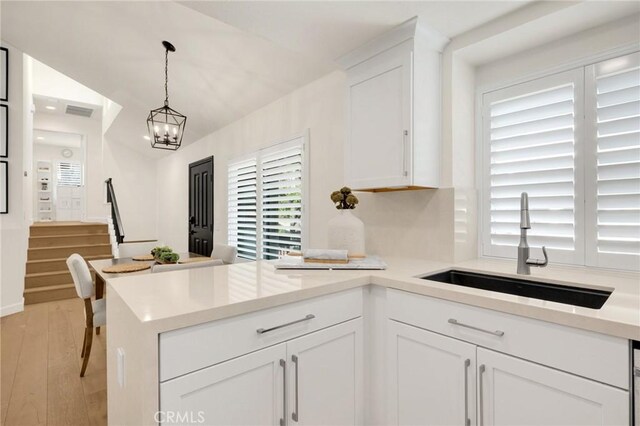 kitchen with decorative light fixtures, white cabinetry, sink, light hardwood / wood-style floors, and an inviting chandelier