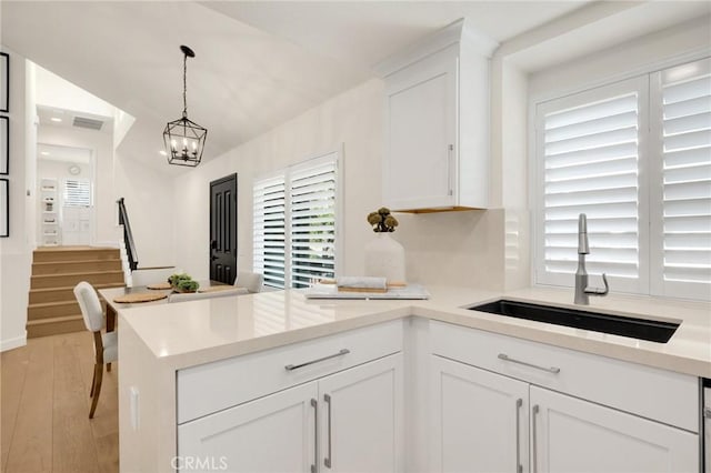 kitchen featuring sink, white cabinetry, hanging light fixtures, a notable chandelier, and light hardwood / wood-style floors