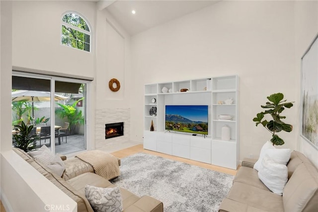 living room with beamed ceiling, a tiled fireplace, high vaulted ceiling, and light hardwood / wood-style flooring