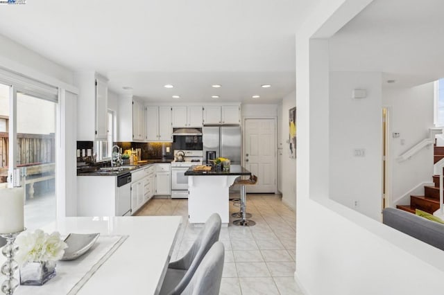 kitchen with a kitchen bar, stainless steel fridge, white range with gas cooktop, dishwashing machine, and white cabinets