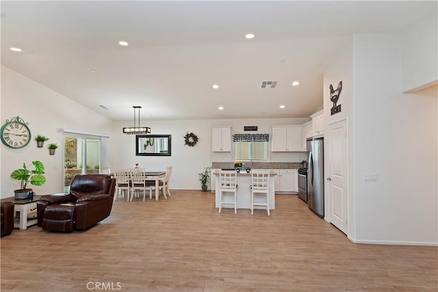 kitchen with a kitchen bar, white cabinetry, light wood-type flooring, appliances with stainless steel finishes, and a kitchen island