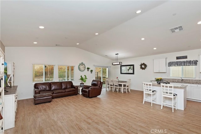 living room featuring lofted ceiling, sink, and light hardwood / wood-style flooring