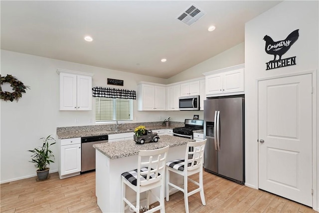 kitchen with white cabinetry, light stone counters, a kitchen island, and appliances with stainless steel finishes