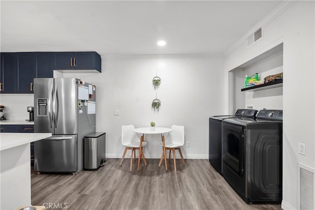 kitchen featuring blue cabinets, ornamental molding, light hardwood / wood-style floors, stainless steel fridge with ice dispenser, and washing machine and dryer