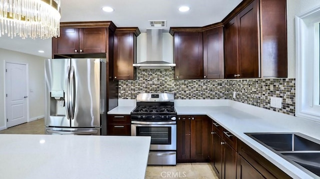 kitchen with sink, hanging light fixtures, appliances with stainless steel finishes, wall chimney range hood, and backsplash