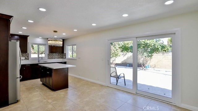 kitchen featuring a kitchen island, decorative light fixtures, sink, stainless steel fridge, and backsplash