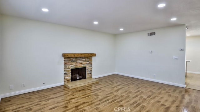 unfurnished living room with hardwood / wood-style flooring and a stone fireplace