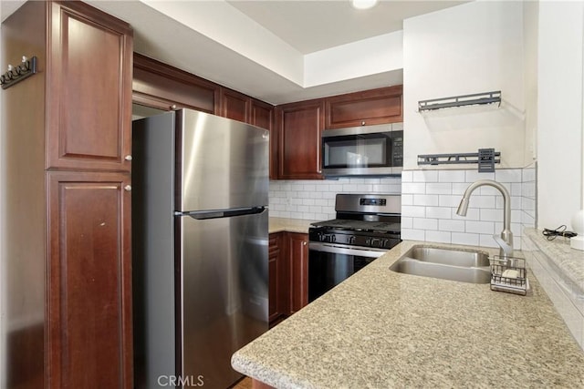 kitchen featuring light stone countertops, appliances with stainless steel finishes, sink, and backsplash