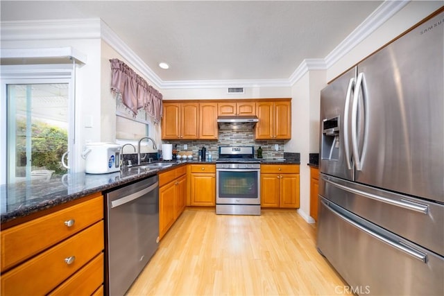 kitchen with sink, tasteful backsplash, light wood-type flooring, appliances with stainless steel finishes, and dark stone counters