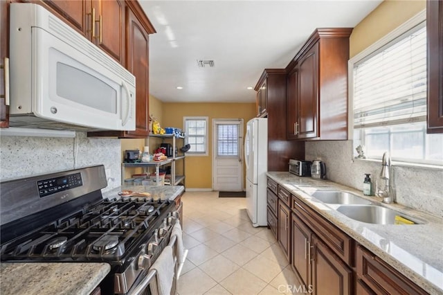 kitchen with sink, light stone counters, light tile patterned floors, white appliances, and backsplash