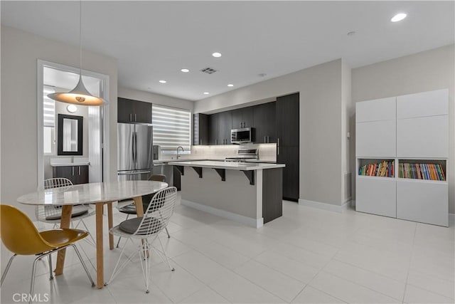 kitchen featuring hanging light fixtures, a kitchen island, appliances with stainless steel finishes, and a kitchen bar