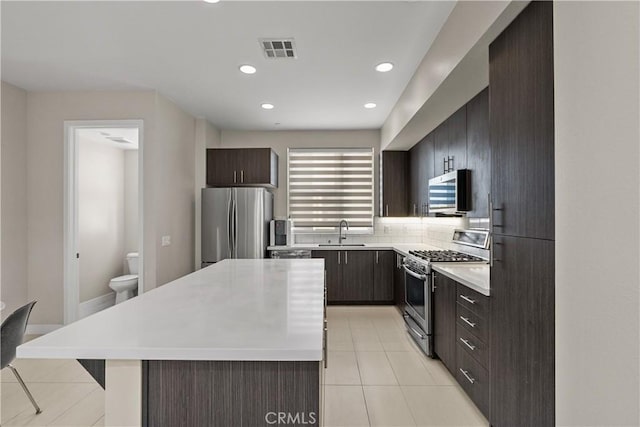 kitchen featuring sink, tasteful backsplash, a center island, light tile patterned floors, and stainless steel appliances