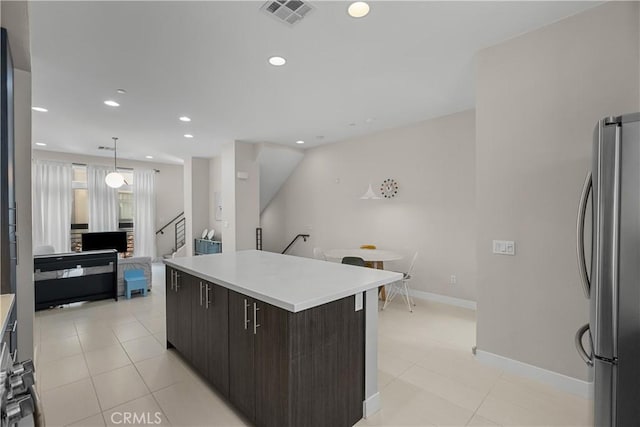 kitchen featuring stainless steel refrigerator, hanging light fixtures, a center island, light tile patterned floors, and dark brown cabinetry