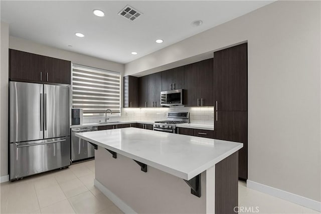 kitchen with appliances with stainless steel finishes, a breakfast bar, sink, decorative backsplash, and a center island