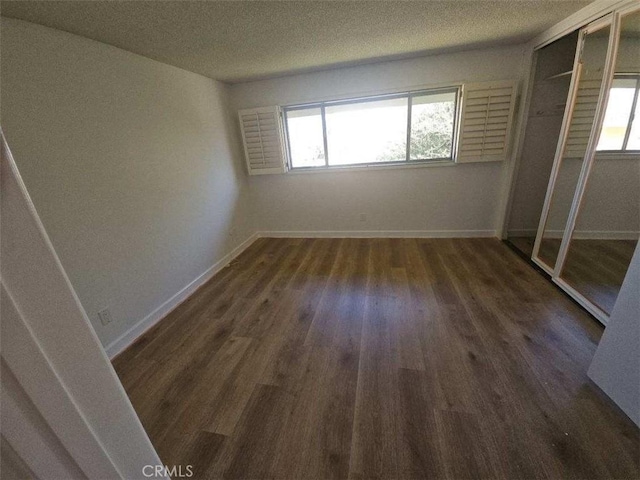 unfurnished bedroom featuring a closet, a textured ceiling, baseboards, and wood finished floors