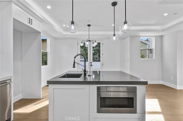 kitchen featuring sink, white cabinetry, hanging light fixtures, a tray ceiling, and light wood-type flooring