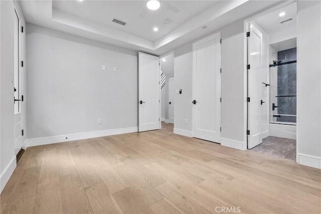 unfurnished bedroom featuring connected bathroom, a raised ceiling, and light hardwood / wood-style floors