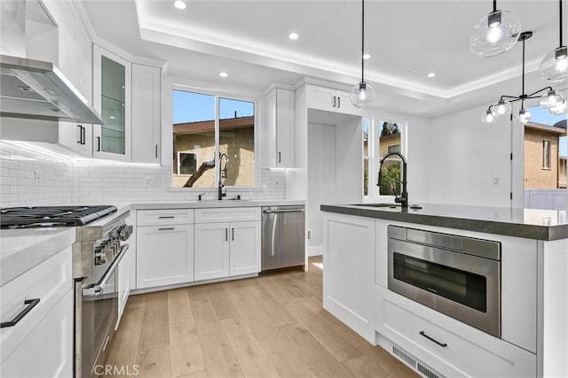 kitchen featuring a tray ceiling, white cabinets, and wall chimney exhaust hood