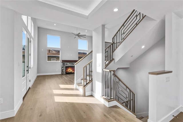 entrance foyer with ceiling fan, a towering ceiling, a fireplace, and light hardwood / wood-style flooring