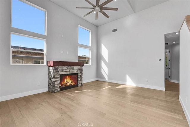 living room with a stone fireplace, light hardwood / wood-style flooring, ceiling fan, and a high ceiling