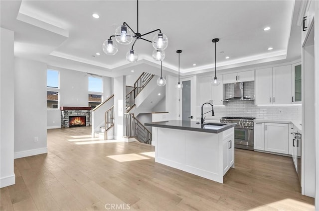 kitchen with high end range, a raised ceiling, sink, and wall chimney range hood