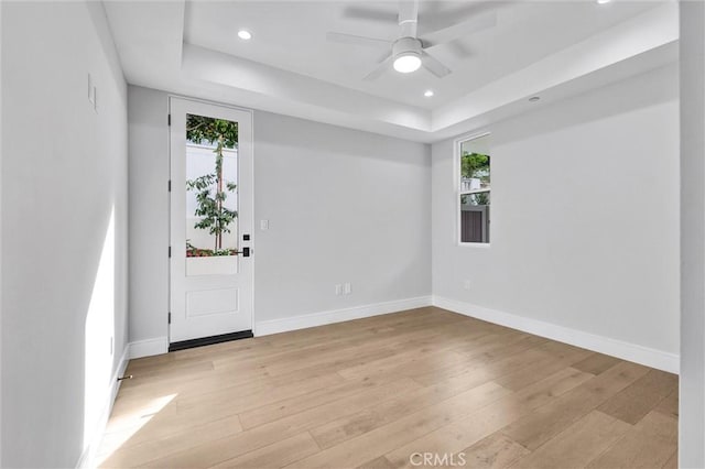 spare room with a raised ceiling, ceiling fan, and light wood-type flooring