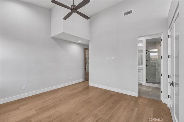 empty room featuring a high ceiling, ceiling fan, and light hardwood / wood-style flooring