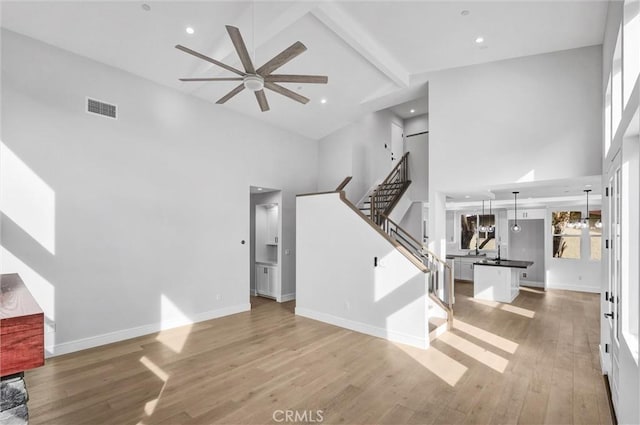 unfurnished living room with ceiling fan, beam ceiling, high vaulted ceiling, and light wood-type flooring