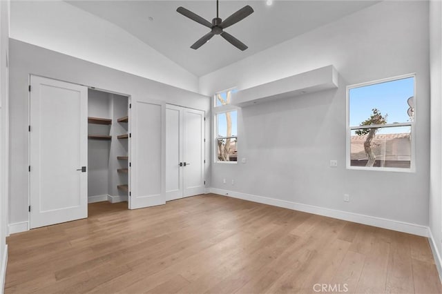 unfurnished bedroom featuring lofted ceiling, light hardwood / wood-style flooring, multiple windows, and two closets