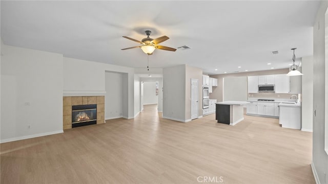 unfurnished living room featuring sink, a fireplace, ceiling fan, and light hardwood / wood-style flooring