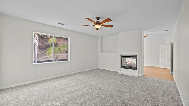 unfurnished living room featuring ceiling fan, a multi sided fireplace, and light carpet