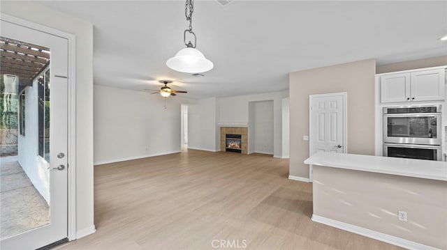 kitchen featuring pendant lighting, white cabinetry, a tiled fireplace, stainless steel double oven, and light hardwood / wood-style flooring