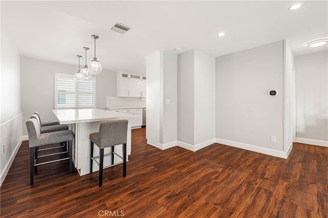 kitchen with pendant lighting, white cabinets, a kitchen breakfast bar, decorative backsplash, and dark wood-type flooring